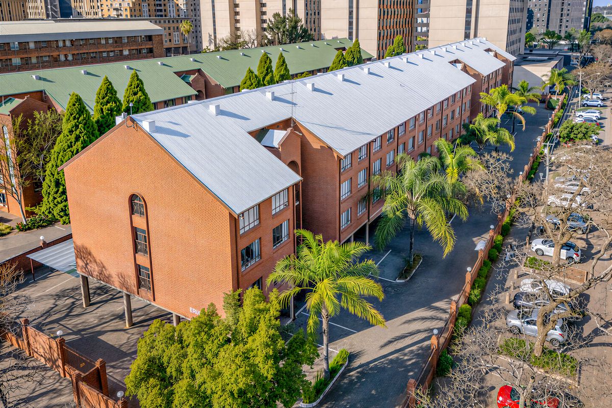 Aerial view of a multi-story brick apartment complex featuring a metal roof, paved driveway, and perimeter wall security.