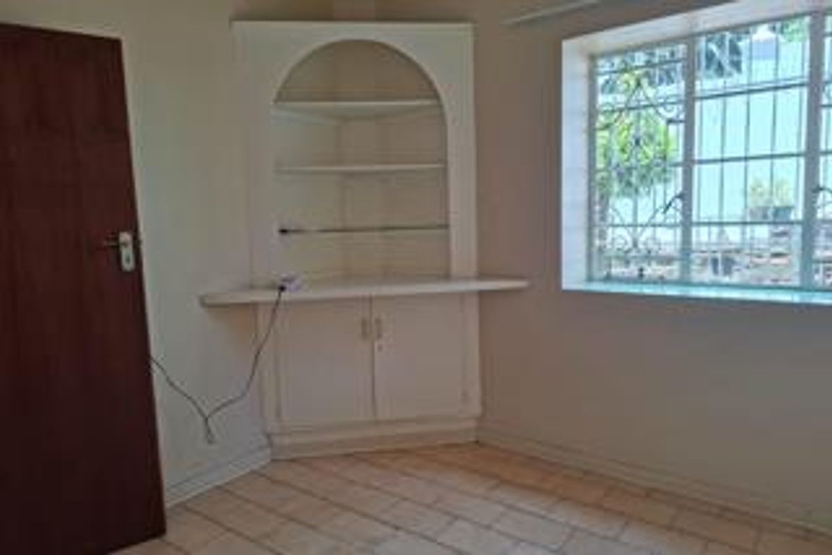 An empty living area featuring a built-in corner display unit, tiled flooring, and a window fitted with security bars.