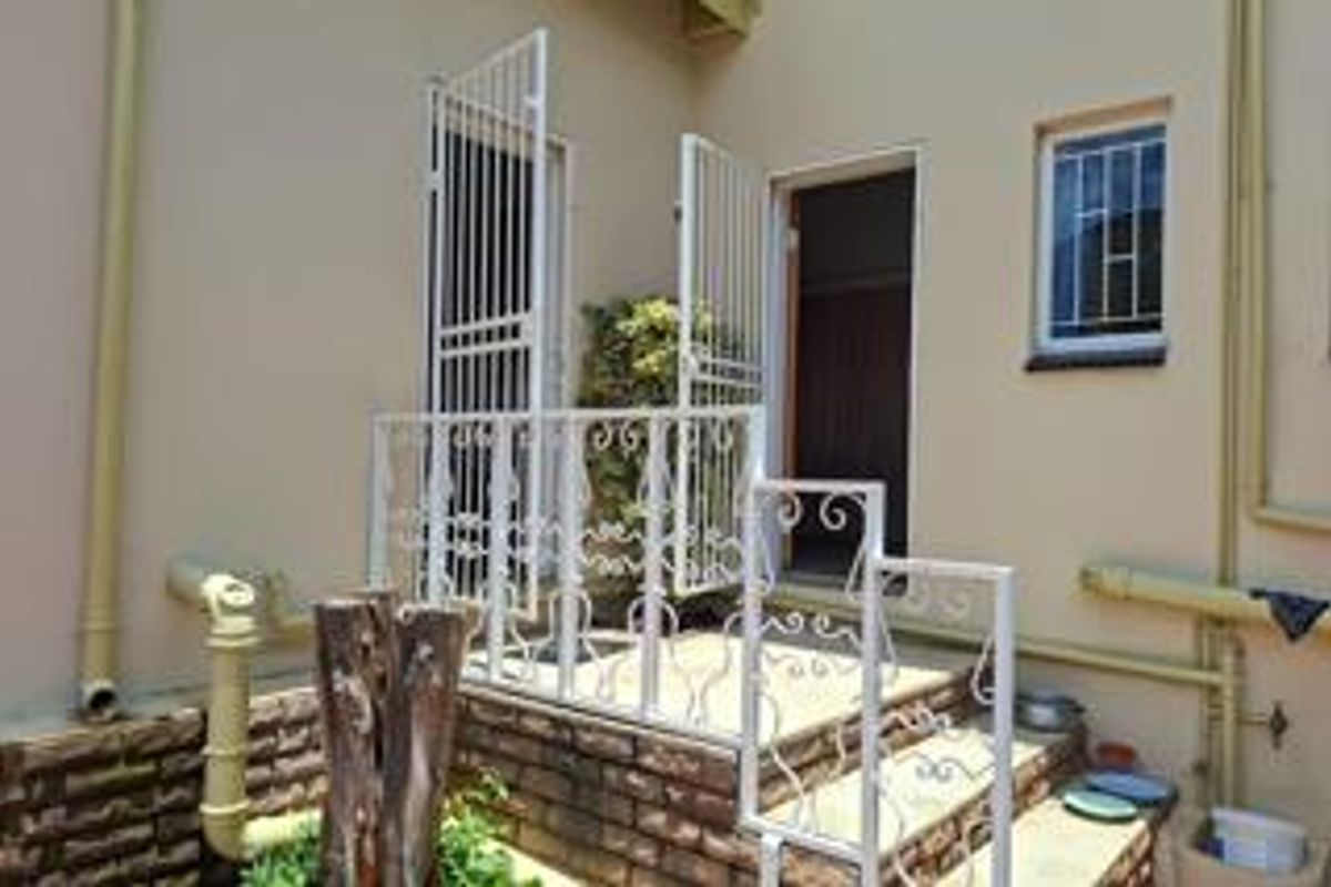 Rear exterior view of the property featuring brick steps, wrought iron security gates, and railings with visible exterior plumbing.