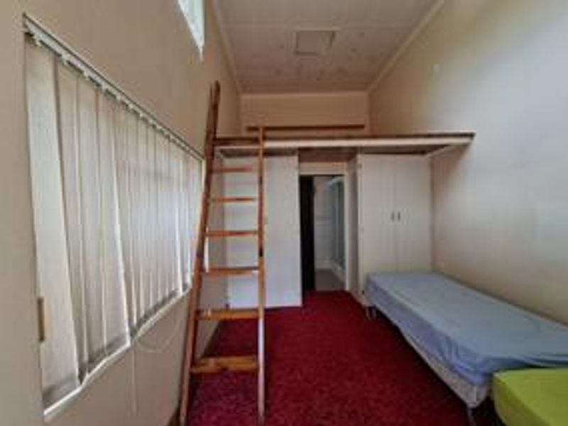 Bedroom featuring a mezzanine loft level with ladder access, built-in cupboards, and vertical blinds.
