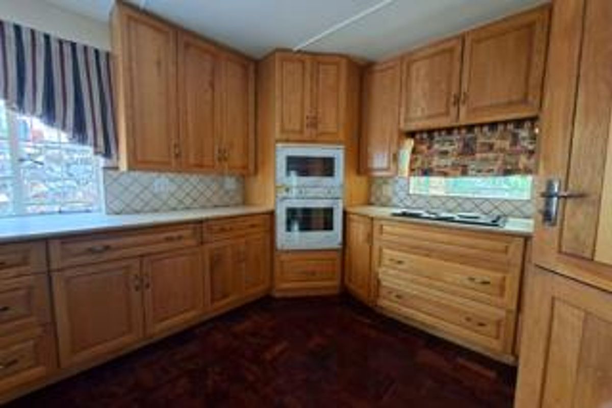 A traditional kitchen featuring extensive wooden cabinetry, a built-in double oven, a hob, and classic parquet flooring.