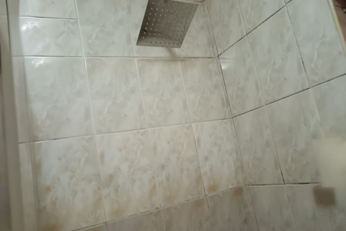 A close-up view of a shower enclosure featuring a square rainfall shower head and tiled walls with visible signs of wear and staining.