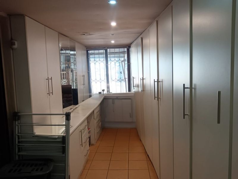 A functional laundry room featuring extensive built-in cabinetry, tiled flooring, and a window with security bars, requiring minor ceiling repairs.