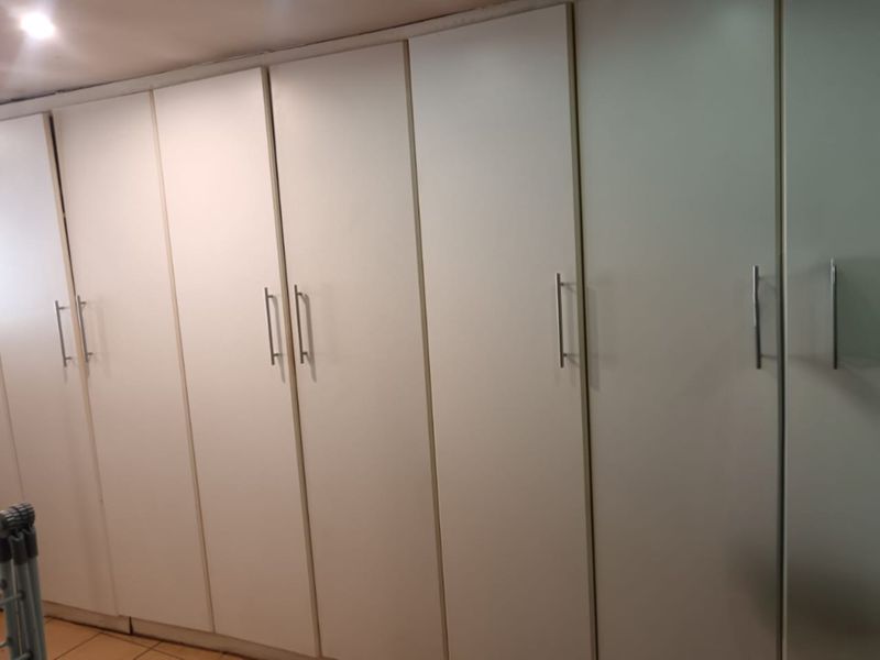 A bedroom featuring a wall of floor-to-ceiling built-in cupboards with modern handles, providing ample storage space.