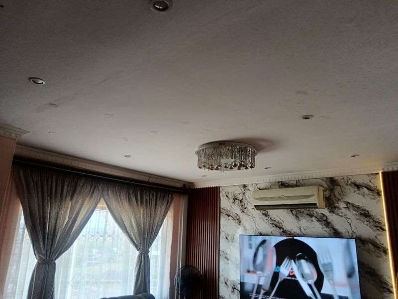 Living room featuring decorative cornice, marble-effect wall cladding, timber slat paneling, and a crystal chandelier, showing signs of ceiling water damage.