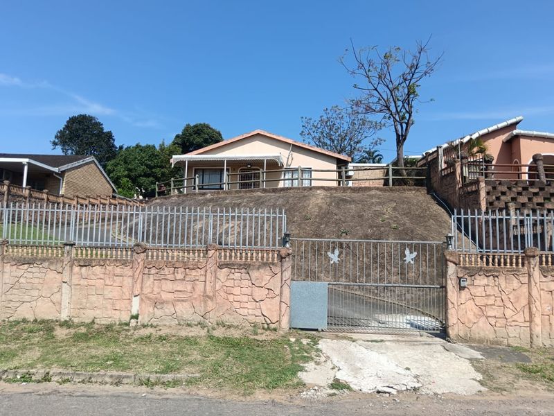 Front elevation of a residential house featuring a raised position, perimeter wall with metal fencing, security gate, and a covered front patio area.