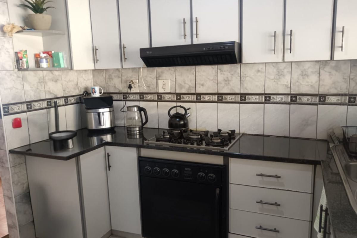 A functional kitchen featuring white cabinetry, dark granite countertops, a gas hob, built-in oven, and a decorative tiled backsplash.