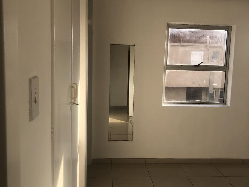 An empty bedroom featuring tiled flooring, built-in cupboards, and a window with natural light.