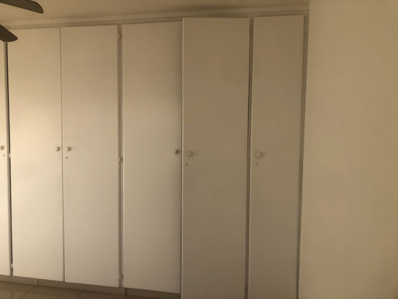 A bedroom interior featuring floor-to-ceiling built-in cupboards and a ceiling fan.