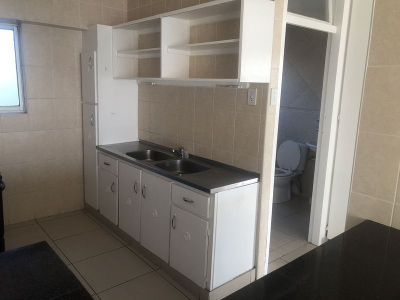 A functional kitchen area featuring built-in cabinetry, a stainless steel double sink, and tiled finishes, with an adjacent bathroom visible.