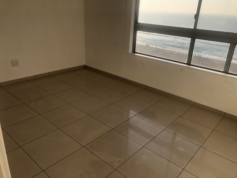 An empty bedroom featuring tiled flooring and a large window offering expansive ocean views.