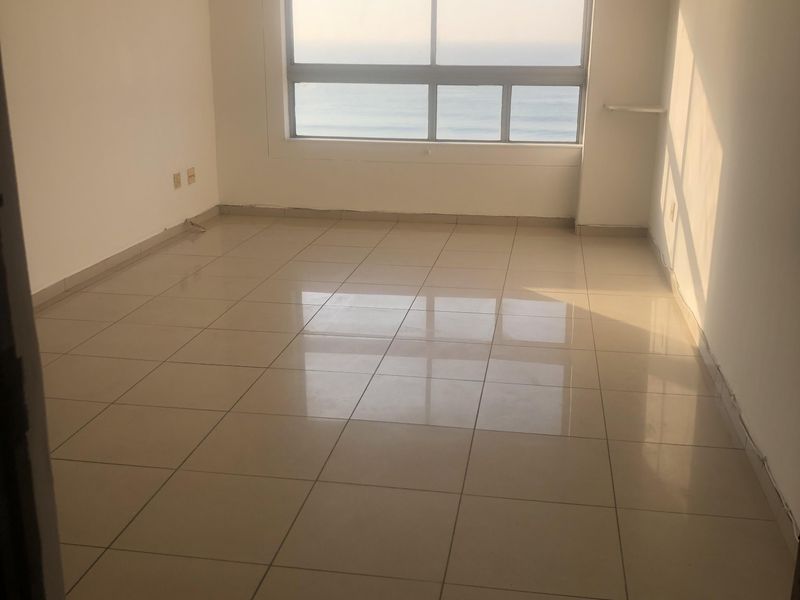 An empty living room featuring tiled flooring, a ceiling fan, and a large window with ocean views.