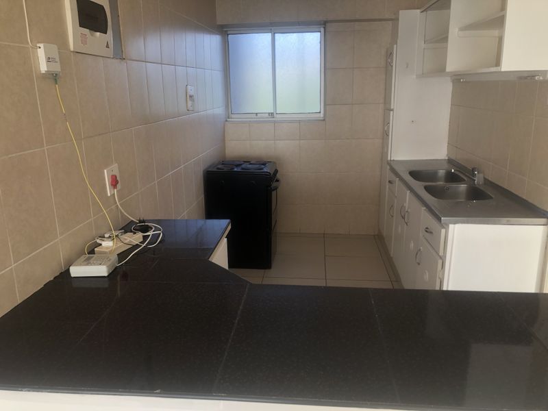 A functional kitchen featuring black granite countertops, double sink, tiled walls, and a freestanding electric stove, offering a blank canvas for renovation.