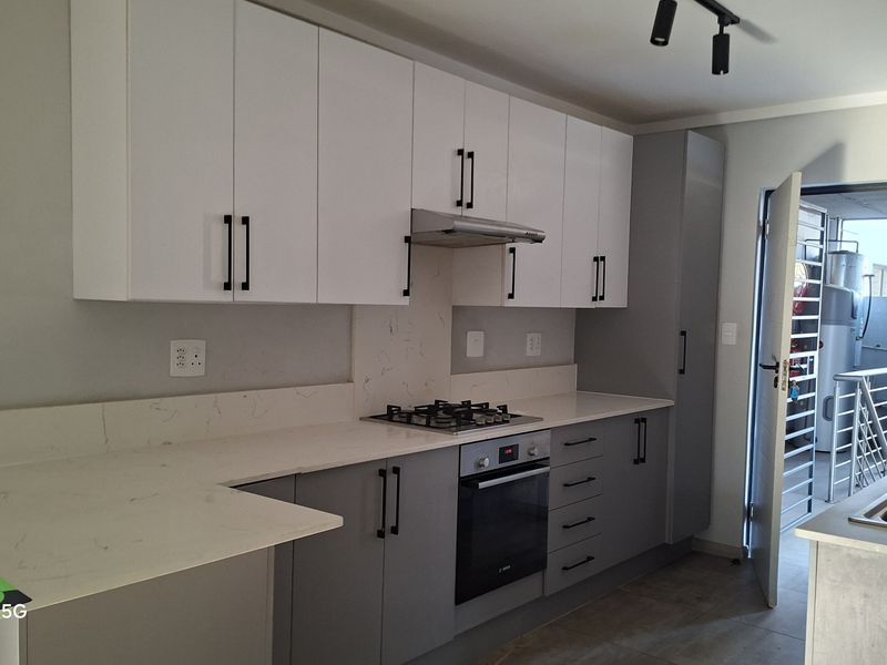 Modern kitchen featuring white upper cabinets, grey lower cabinetry, stone countertops, gas hob, built-in oven, and integrated sink.