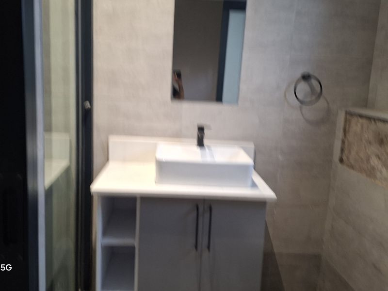 A bathroom featuring a modern vessel sink vanity, wall mirror, and towel ring, currently showing unfinished wall tiling requiring repair.