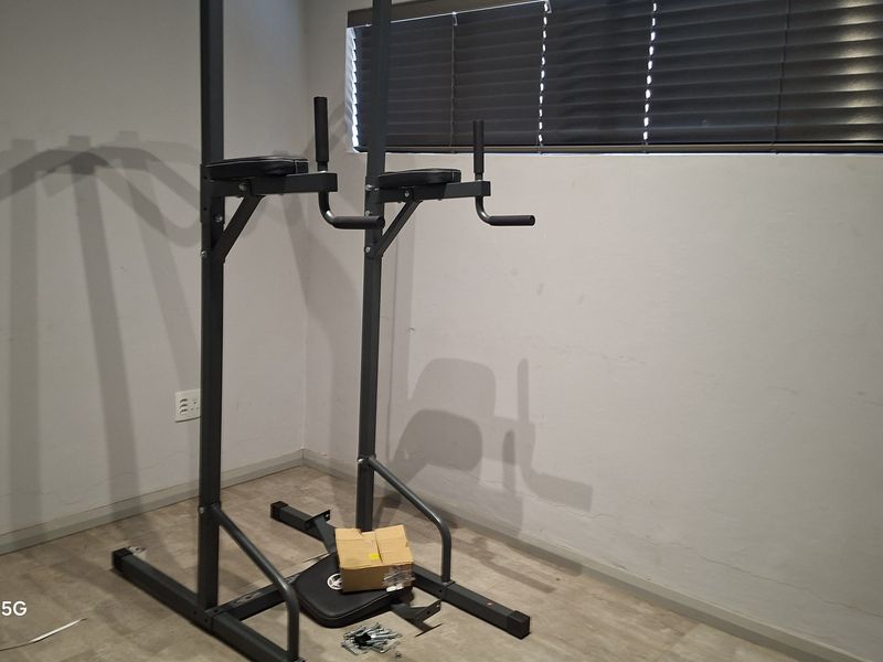 A small room currently utilized as a home gym, featuring neutral walls, wood-look flooring, and venetian blinds.