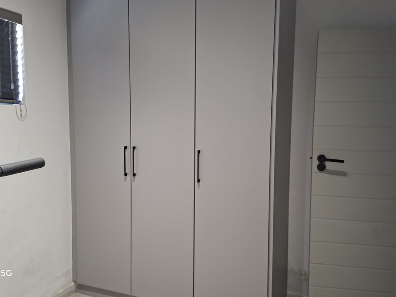 A clean bedroom featuring modern built-in cupboards and a neutral interior door.