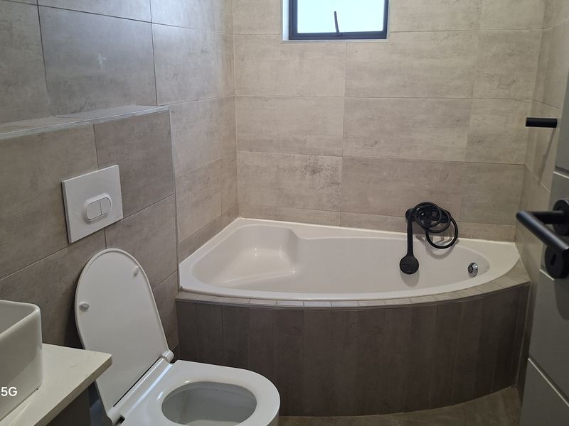 Modern bathroom featuring a corner bathtub, wall-mounted toilet with concealed cistern, and neutral large-format wall tiles.
