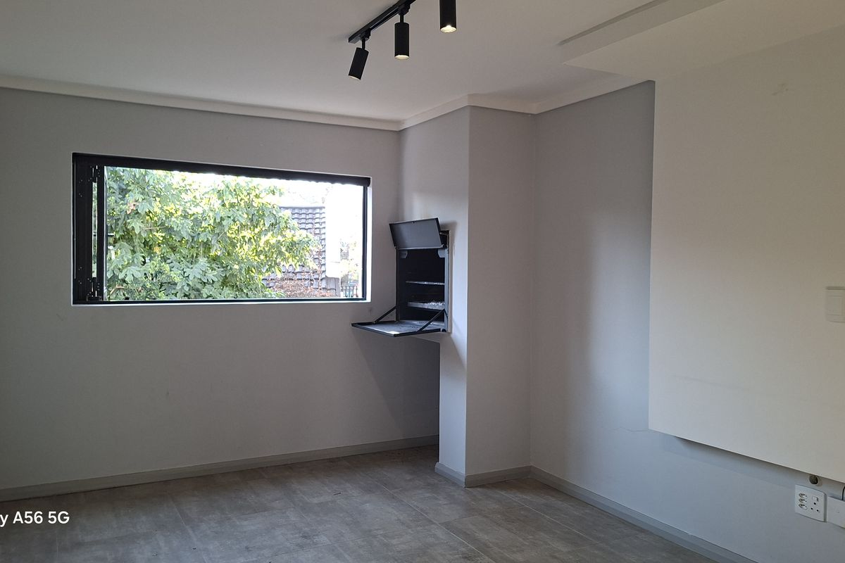 A bright, empty living area featuring modern track lighting, tiled floors, and a convenient built-in braai unit.