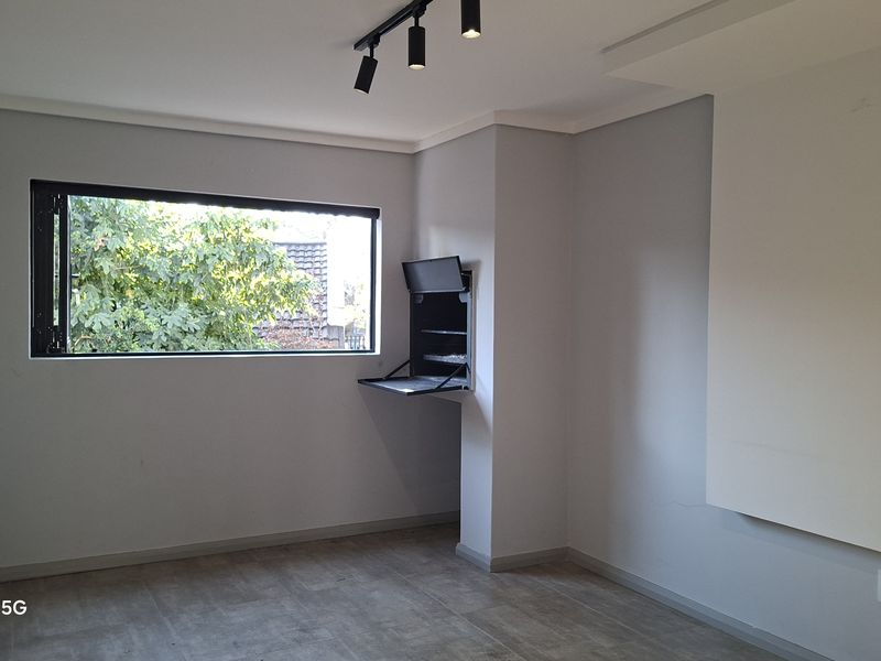 A bright, empty living area featuring modern track lighting, tiled floors, and a convenient built-in braai unit.