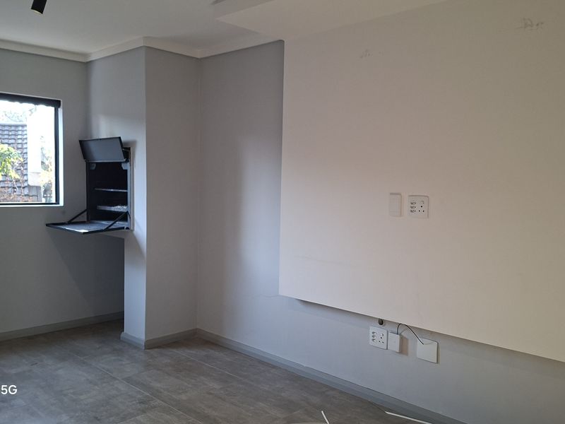 An empty living room featuring tiled flooring, a built-in wall unit, and neutral grey walls, providing a clean canvas for interior design.