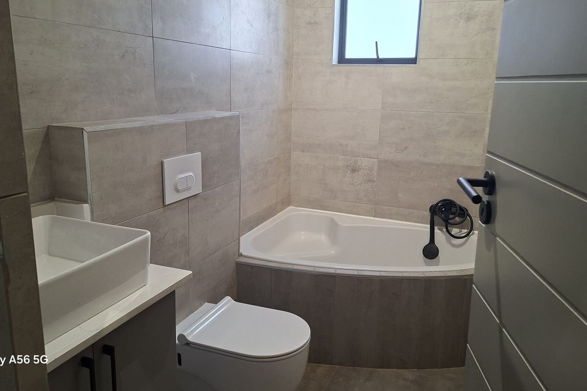 Modern bathroom featuring a built-in bathtub, wall-mounted toilet, and a sleek vanity basin with contemporary tiled finishes.