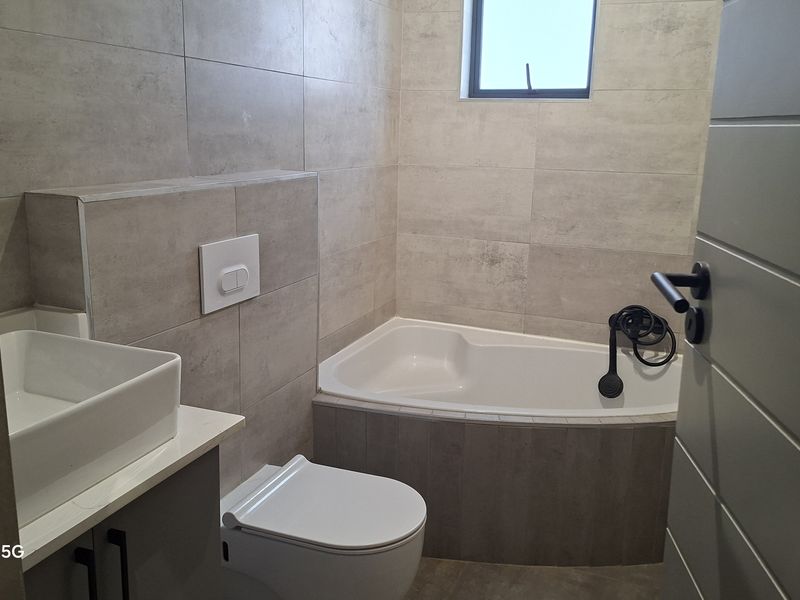 Modern bathroom featuring a built-in bathtub, wall-mounted toilet, and a sleek vanity basin with contemporary tiled finishes.