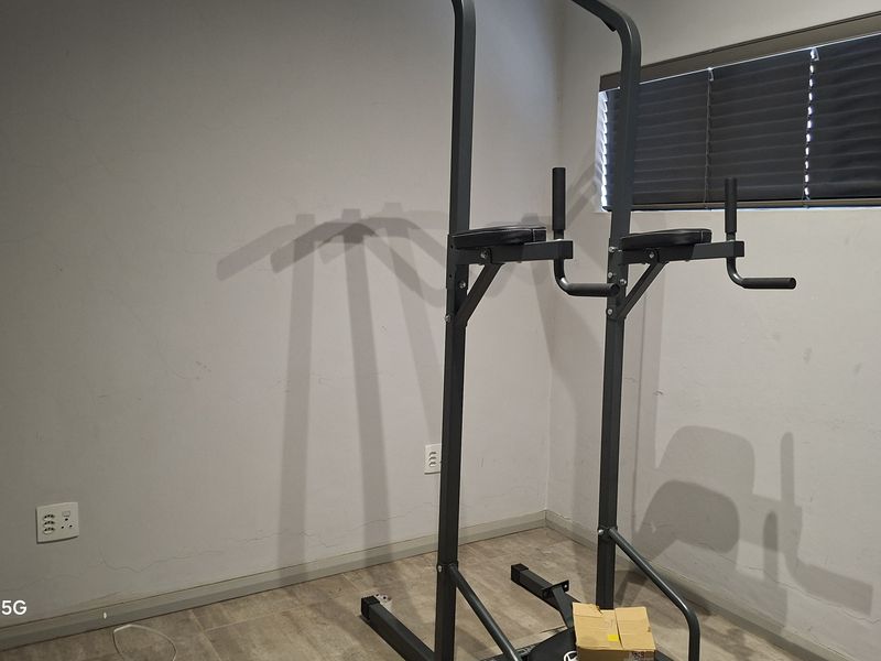 A small room currently used as a home gym, featuring tiled flooring, venetian blinds, and visible wall cracks requiring maintenance.