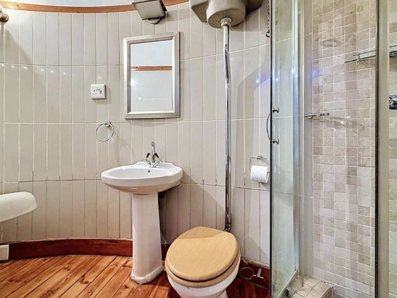 A functional bathroom featuring a pedestal basin, toilet, and separate shower enclosure with tiled walls and timber flooring.