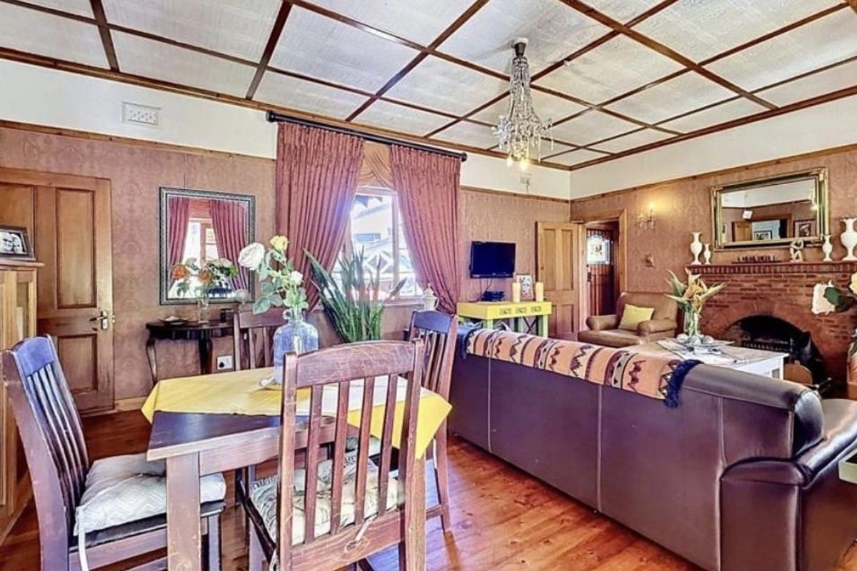 A traditional living room featuring warm timber flooring, a classic brick fireplace, and a distinctive coffered ceiling with a central chandelier.