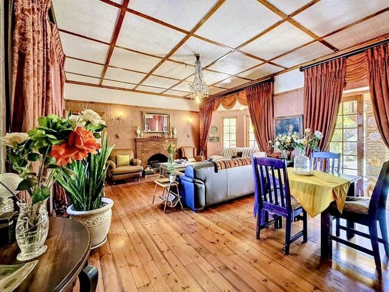 Spacious open-plan living and dining area featuring warm timber flooring, a classic brick fireplace, and a distinctive coffered ceiling with a central chandelier.