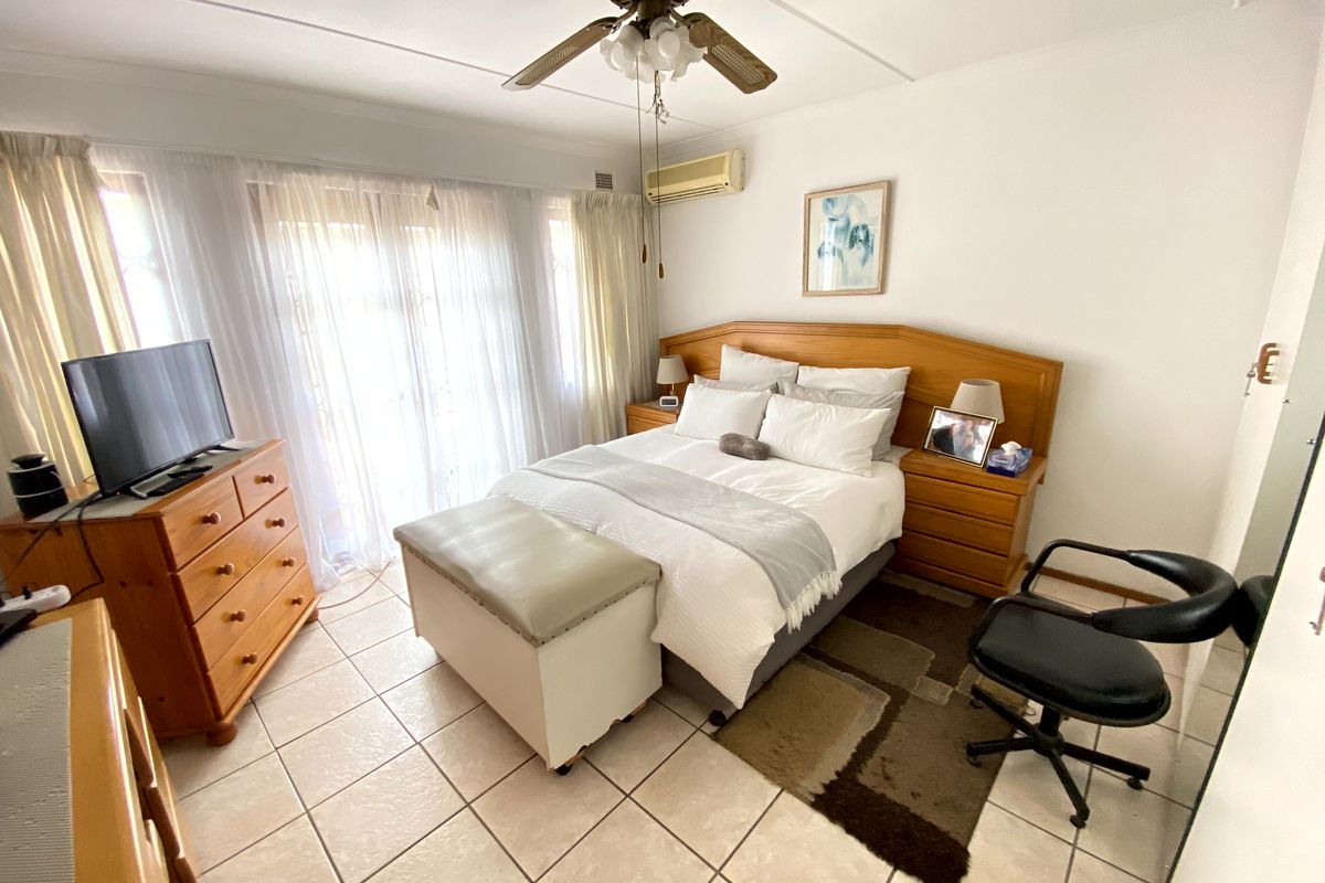 A bedroom featuring tiled flooring, a ceiling fan, and a wall-mounted split-system air conditioner with access to an outdoor area via sliding glass doors.