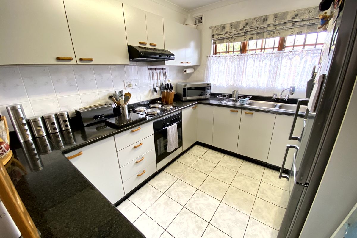A functional kitchen featuring white cabinetry, dark granite countertops, a built-in oven, electric hob, and tiled flooring with a double basin sink.