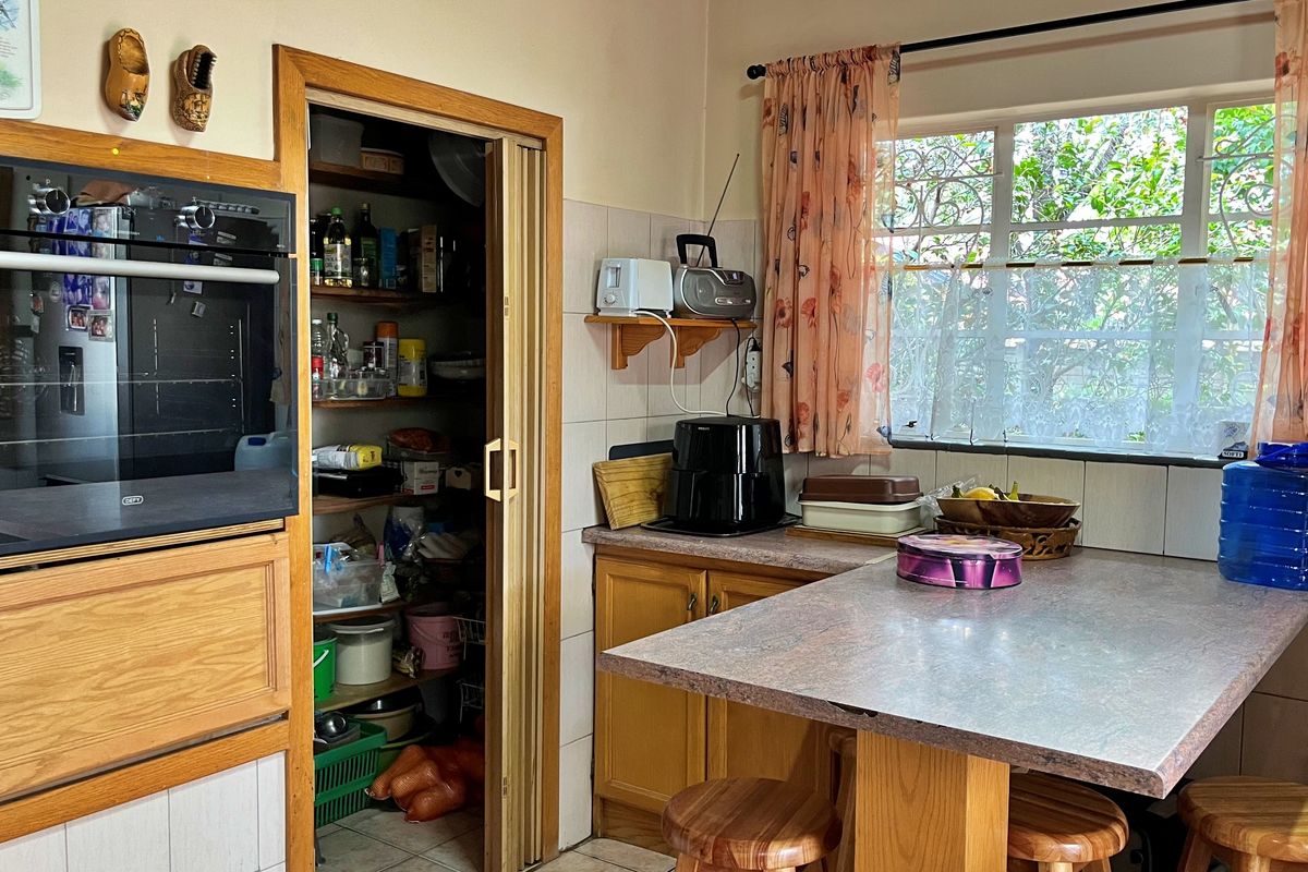 A functional kitchen featuring wooden cabinetry, a built-in oven, and a convenient walk-in pantry with shelving, offering a practical layout for daily meal preparation.