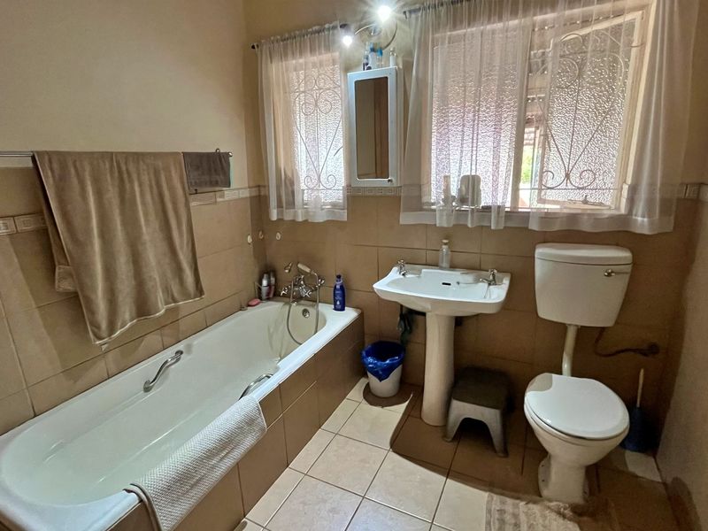 A functional bathroom featuring a bathtub, pedestal basin, and toilet with neutral wall and floor tiling.