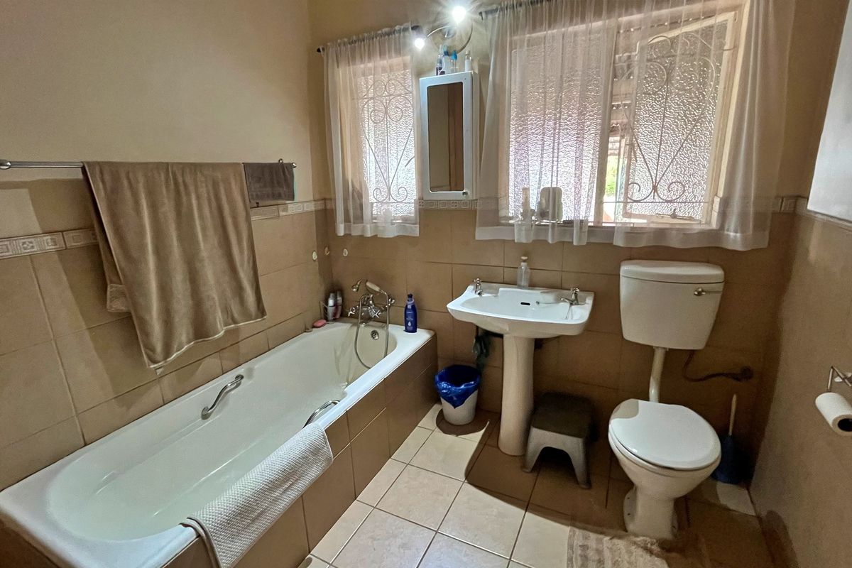 A functional bathroom featuring a bathtub, pedestal basin, and toilet with neutral wall and floor tiling.