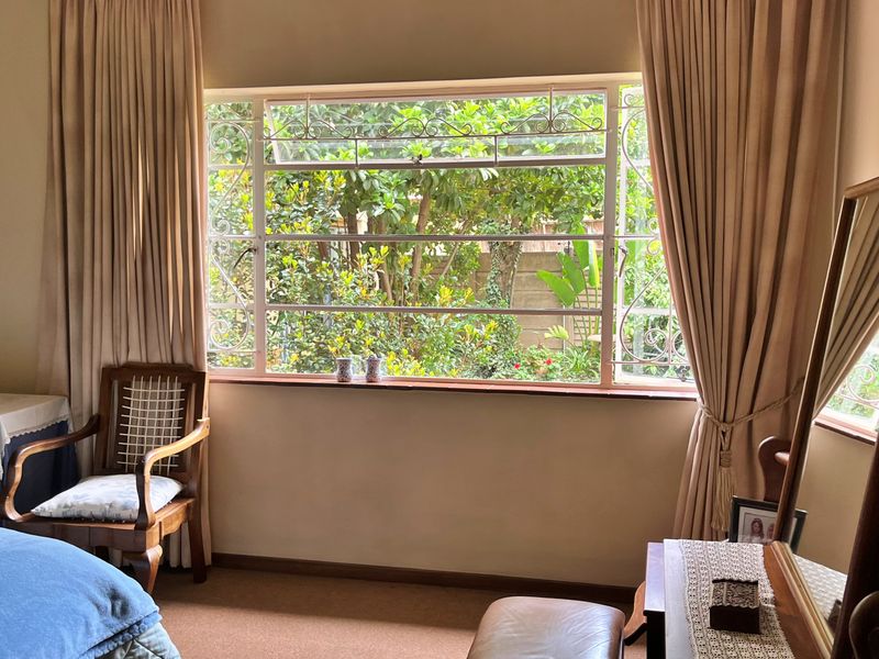 A bedroom featuring a large window with decorative security bars, providing natural light and a view of the garden.