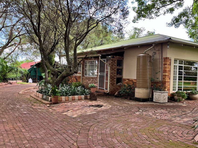 Front exterior view of a single-story house featuring a brick paved driveway, established trees, and a water storage tank.