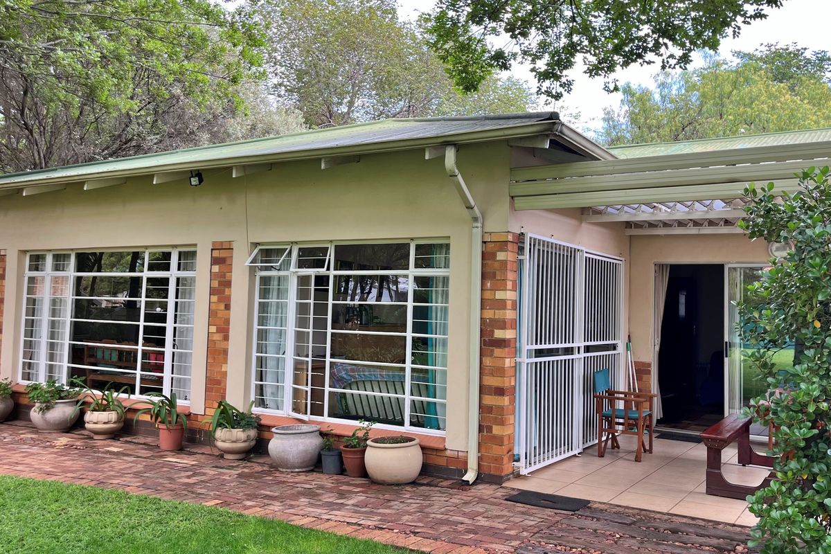 Rear exterior view of the house featuring a paved patio area, security gates, and large windows with metal frames set against a garden.