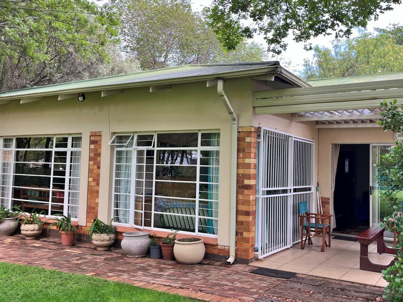 Rear exterior view of the house featuring a paved patio area, security gates, and large windows with metal frames set against a garden.