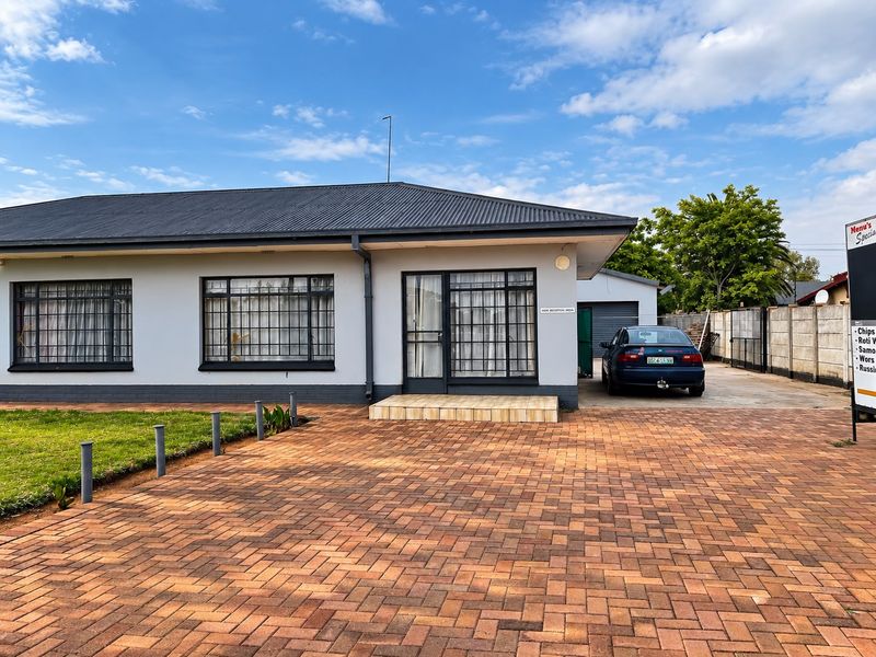 Front exterior view of a single-story house featuring a paved driveway, metal roof, and secure window bars.