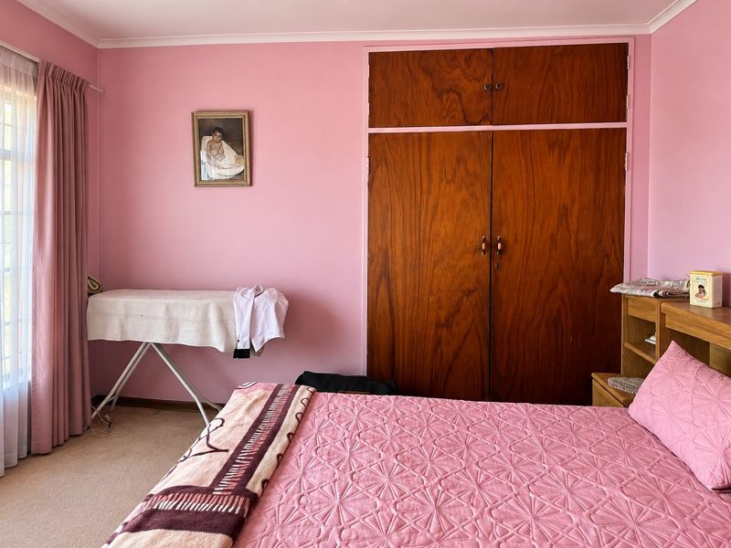 A bedroom featuring built-in wooden wardrobes, carpeted flooring, and large windows with curtains, offering a functional space with potential for modernization.