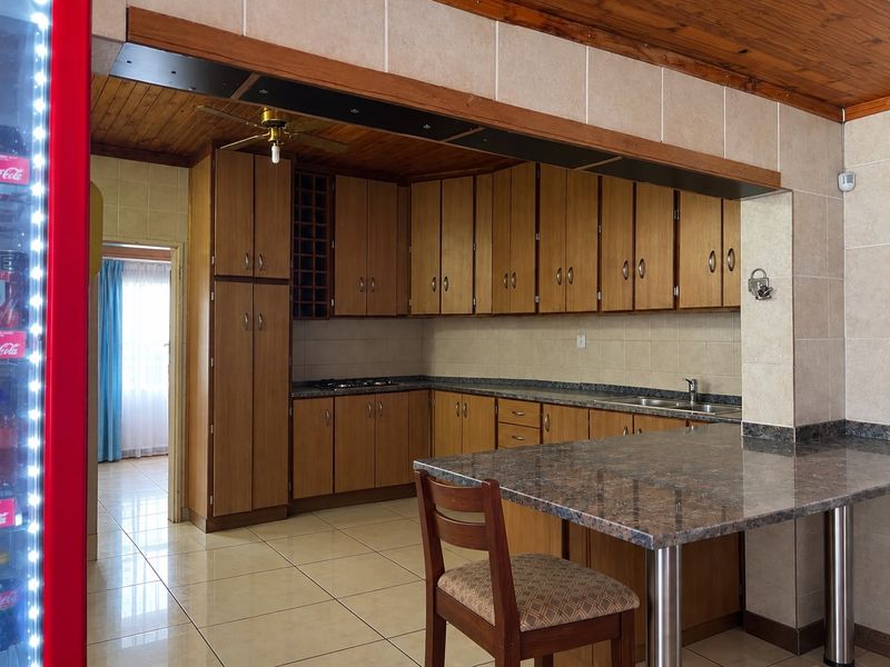 A functional kitchen featuring wooden cabinetry, granite countertops, a breakfast bar, and tiled flooring, with a warm wooden ceiling finish.