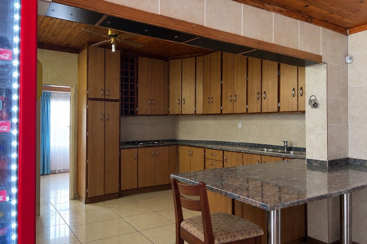 A functional kitchen featuring wooden cabinetry, granite countertops, a breakfast bar, and tiled flooring, with a warm wooden ceiling finish.