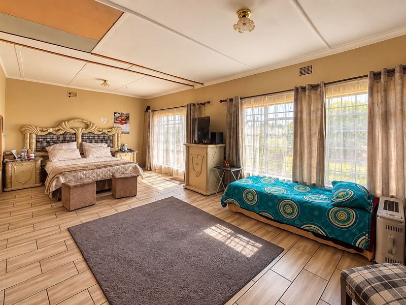 Spacious bedroom featuring tiled flooring and large windows allowing natural light, with visible ceiling paneling requiring maintenance or cosmetic updates.