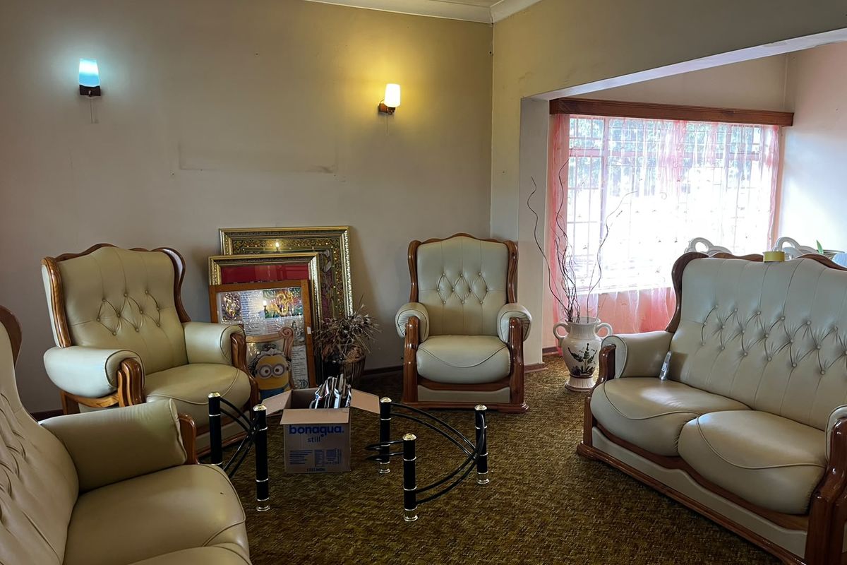 A living room featuring wall-mounted lighting, coving, and a window with security bars, finished with dated carpeting.