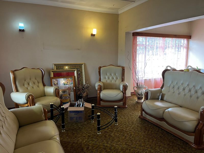 A living room featuring wall-mounted lighting, coving, and a window with security bars, finished with dated carpeting.