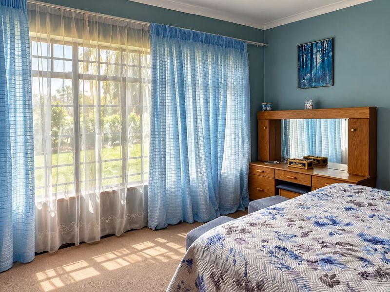 A well-lit bedroom featuring large windows with natural light, carpeted flooring, and coved ceiling details.