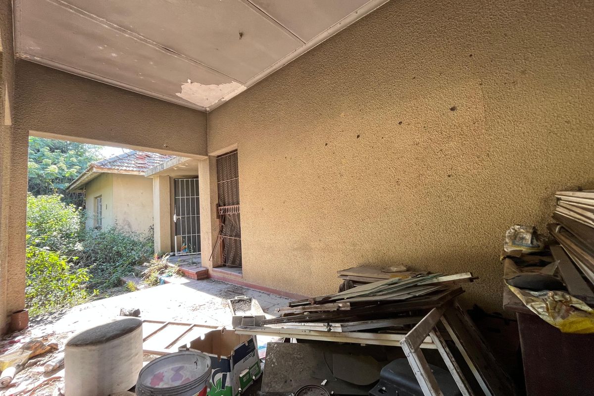 A covered outdoor patio area featuring textured walls and concrete flooring, currently requiring maintenance and clearing of debris.