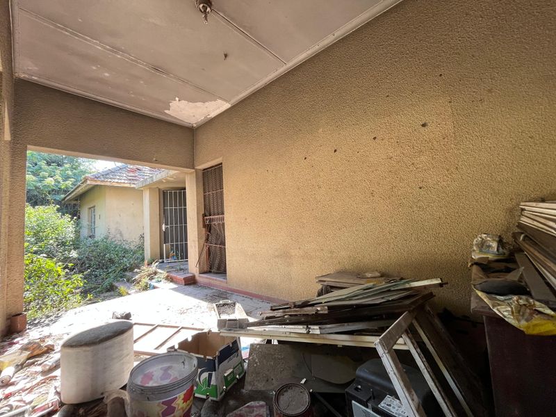 A covered outdoor patio area featuring textured walls and concrete flooring, currently requiring maintenance and clearing of debris.